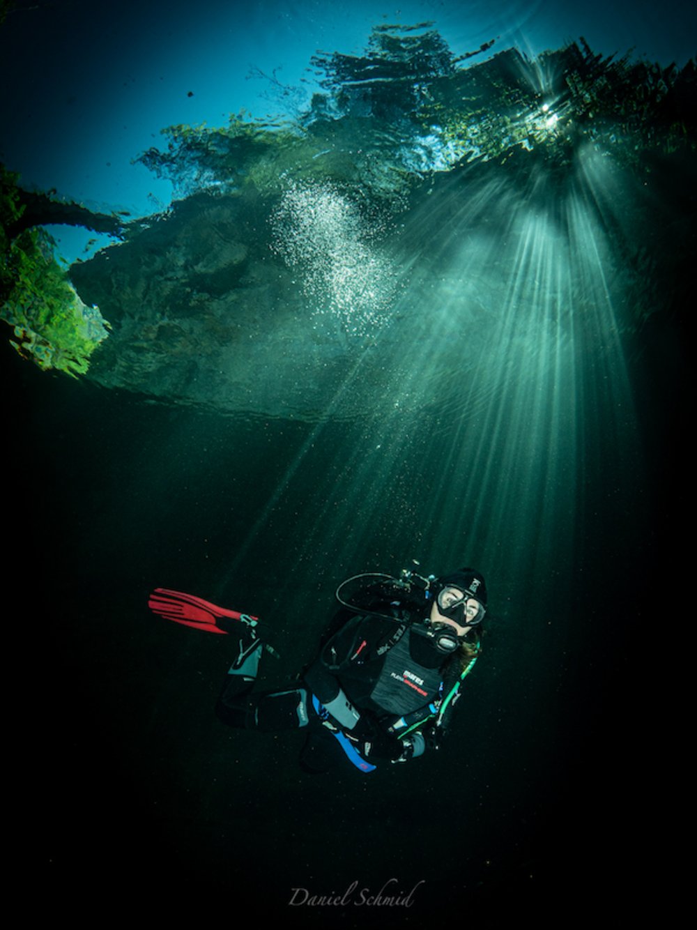 Underwater photography of a diver in a river. The sun shines through the water surface and draws beautiful rays. 